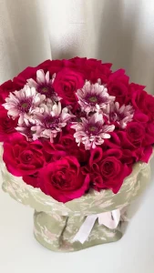 Bouquet of pink roses and white and pink chrysanthemum in green cashmere shawl with artistic flowers decorations and white rubbon.