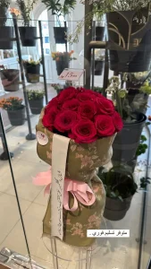 bouquet of pink roses in green cashmere shawl with artistic flowers decorations and pink rubbon. white embroidery with black arabic caligraphy. with label of the shop 7rose om copie.webp