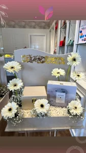 White marble wedding board with golden inscriptions in arabic and gerberas with pebbles and white baby's breath. Luxury box with golden lock and fragrance brand amouage, model reflection